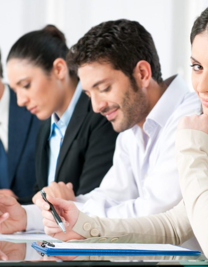 Smiling proud business woman looking at camera with satisfaction and working colleagues in office